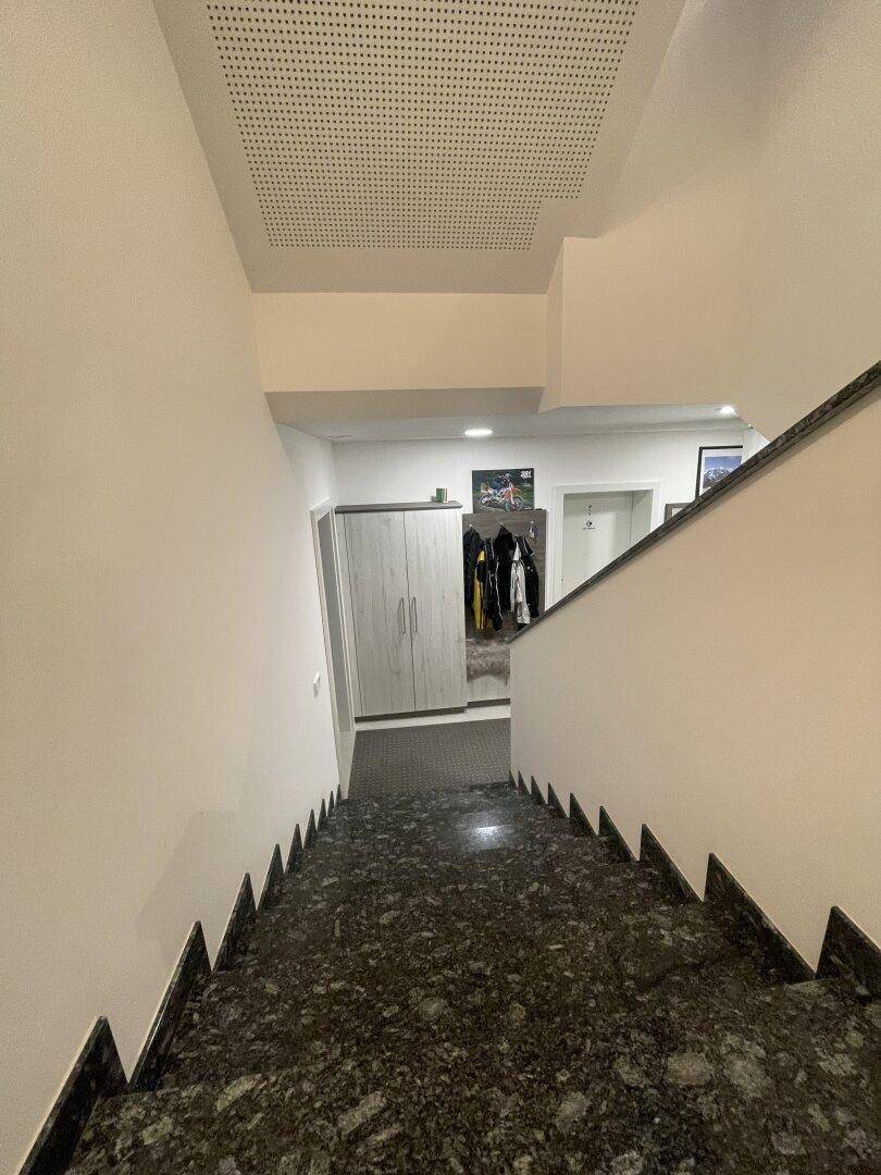 Elegante Treppe mit dunklem Granitbelag und weiß gestrichenen Wänden, beleuchtet von modernen Deckenleuchten.