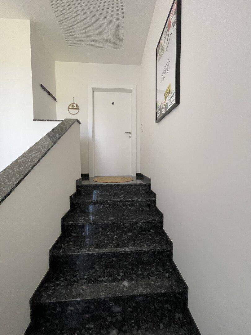 Elegantes Treppenhaus mit dunklen Granitstufen, die zu einer weißen Tür im oberen Bereich führen.