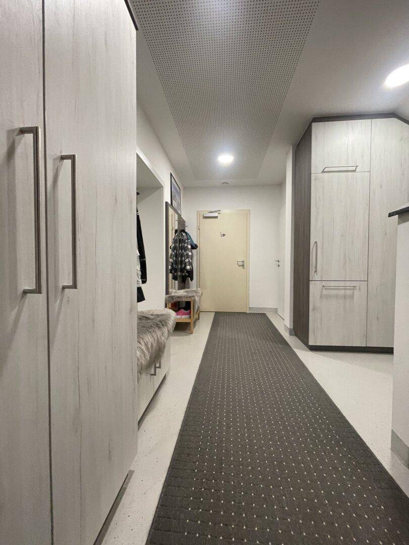 Heller Flur mit integrierten Schränken und Garderobe, ausgestattet mit einem Teppichläufer und moderner Beleuchtung.