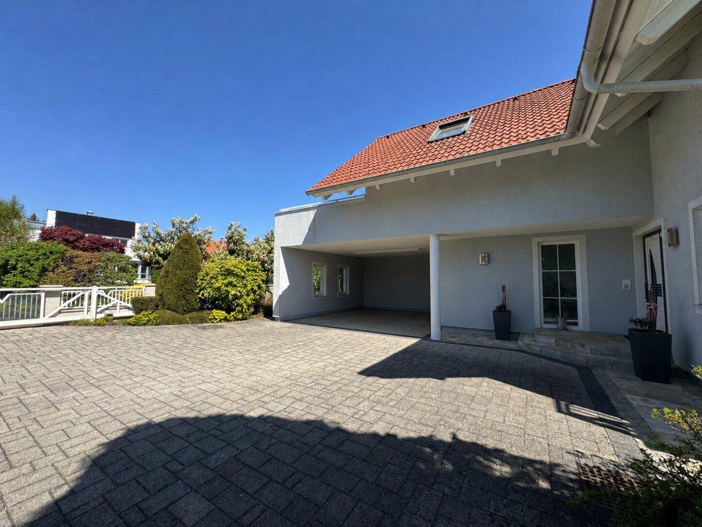 Geräumige Einfahrt mit gepflastertem Bereich und überdachtem Carport am Haus.