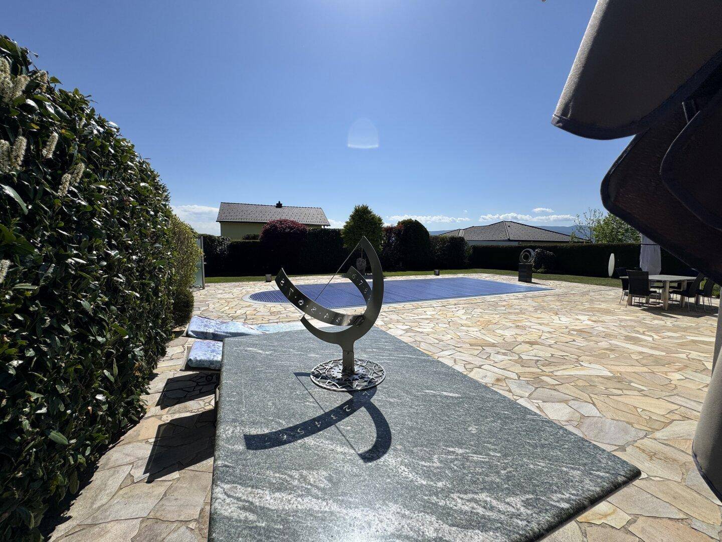 Detailansicht einer Sonnenuhr auf der Steinterrasse mit Blick auf den Poolbereich.