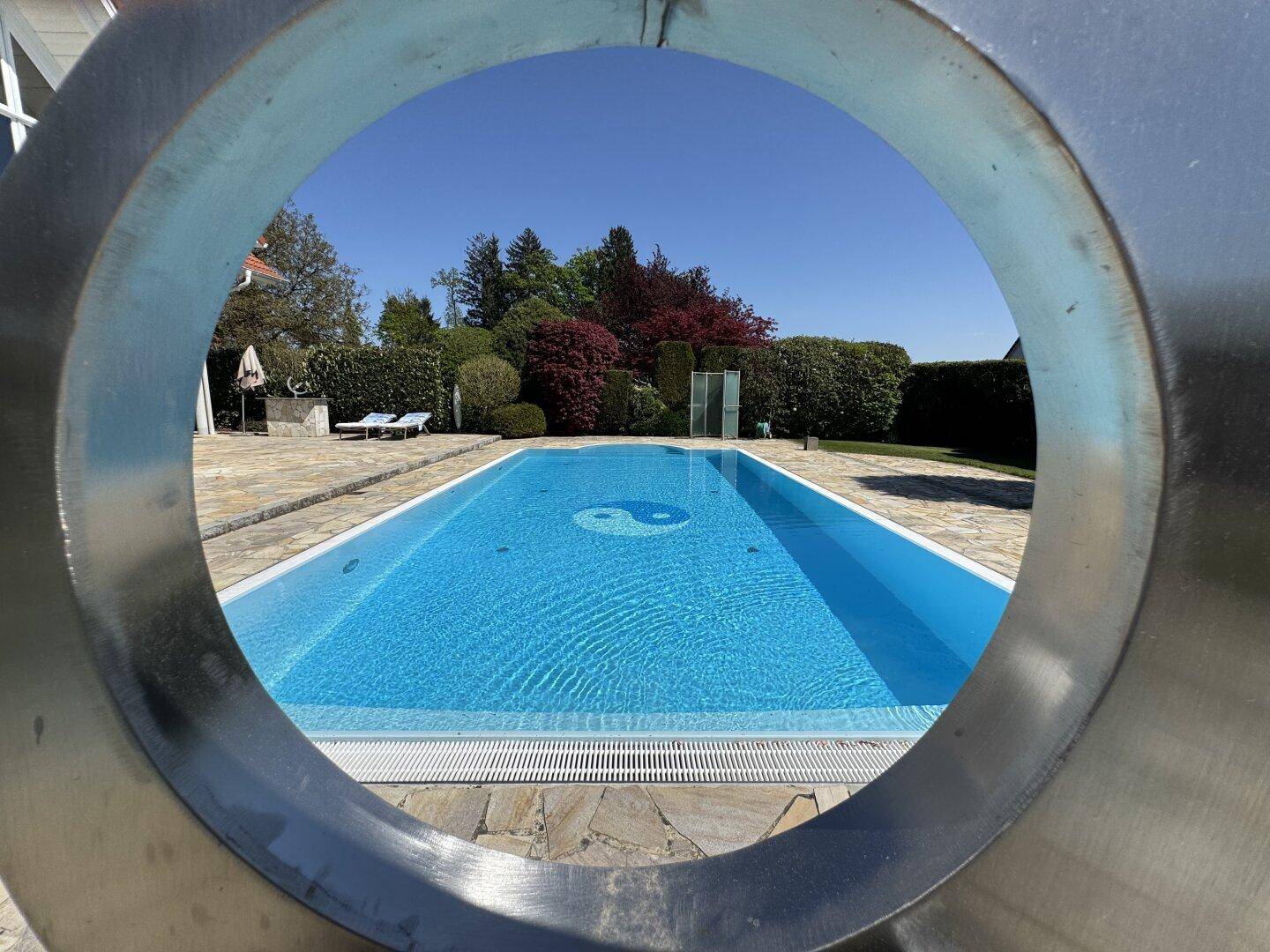 Blick durch eine moderne Skulptur auf den Poolbereich und den dahinterliegenden Garten.