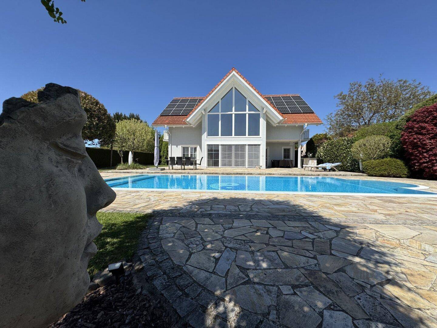 Gartenansicht mit Pool und Hausfassade, umgeben von gepflegten Grünflächen und dekorativen Elementen.