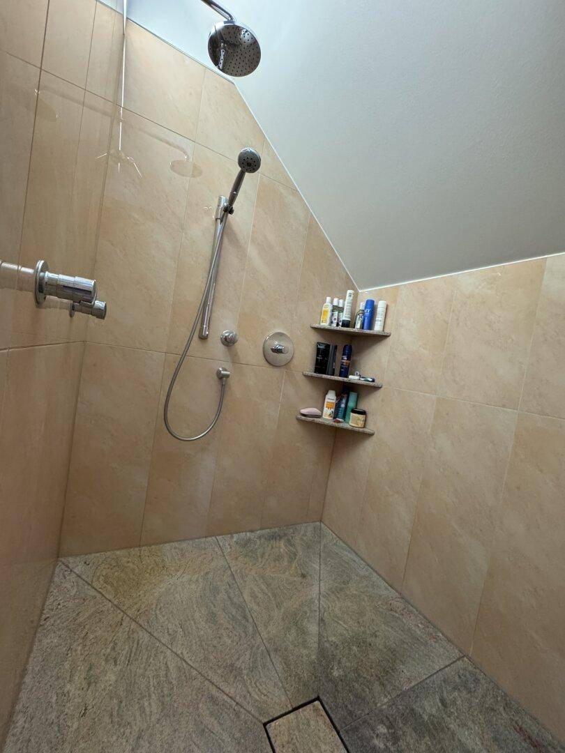 Moderne Duschkabine mit Regendusche und Handbrause, gefliest mit beigen Natursteinfliesen.
