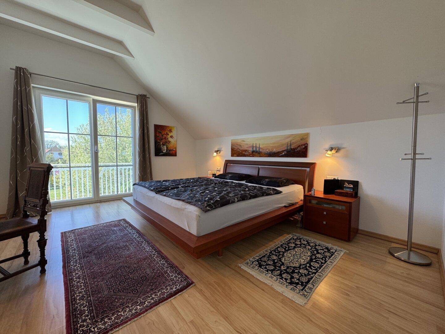 Helles Schlafzimmer im Dachgeschoss mit Holzboden, Doppelbett und Balkonzugang.