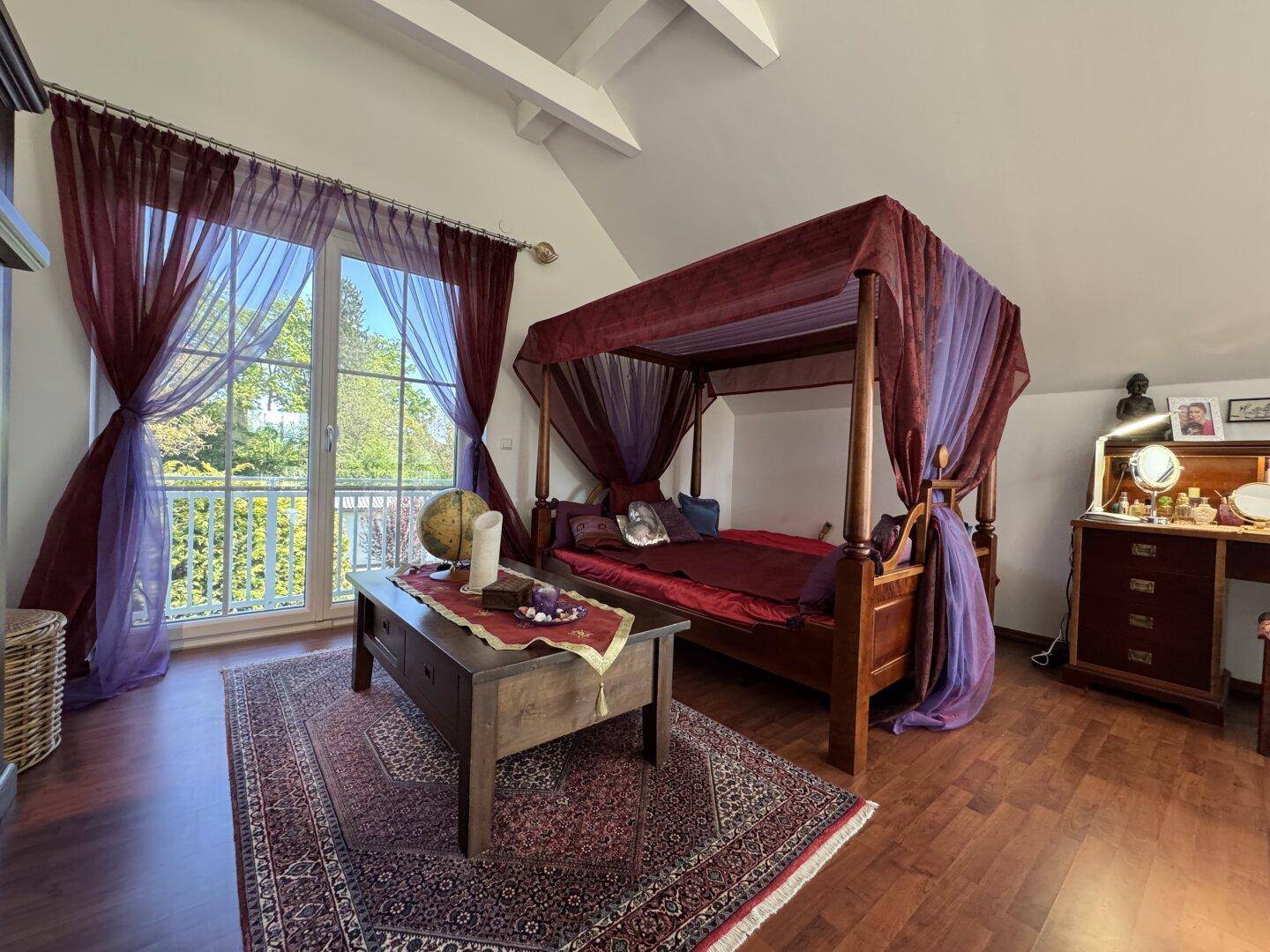 Romantisches Schlafzimmer mit Himmelbett, Holzboden und Zugang zu einem Balkon.