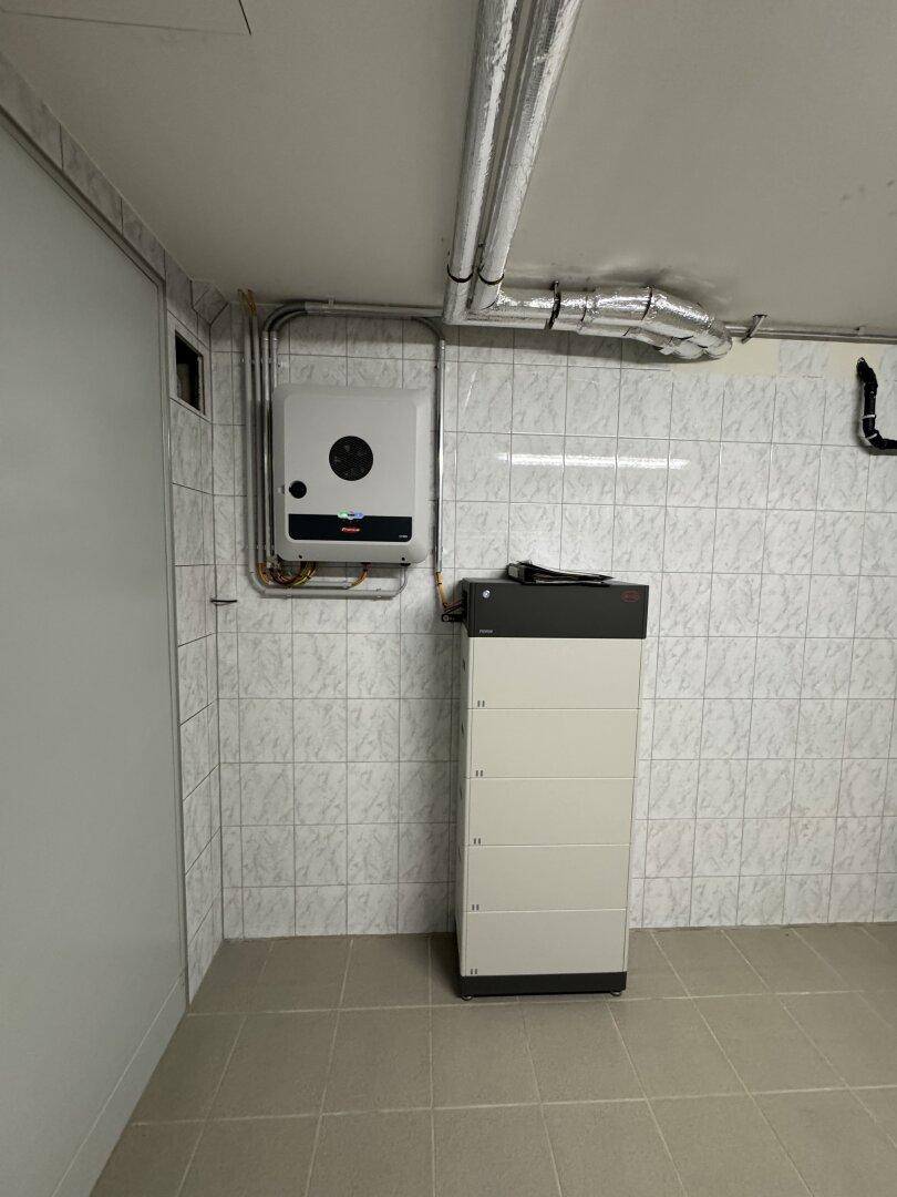 Technikraum mit Photovoltaik-Systemkomponenten und Batteriespeicher, gefliesten Wänden und Boden.