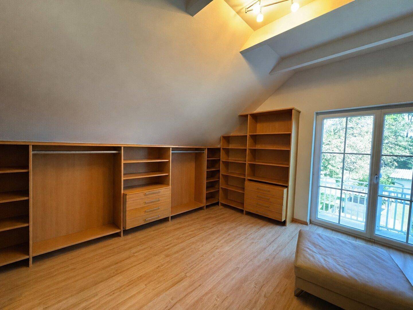 Geräumiger Ankleidebereich mit maßgefertigten Holzschränken und Zugang zum Balkon.