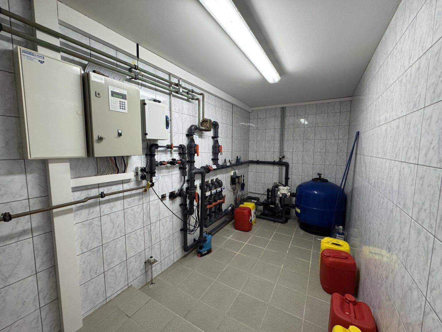 Technikraum mit Wasseraufbereitungs- und Filtersystemen, Pumpen und Kanistern, gefliesten Wänden.