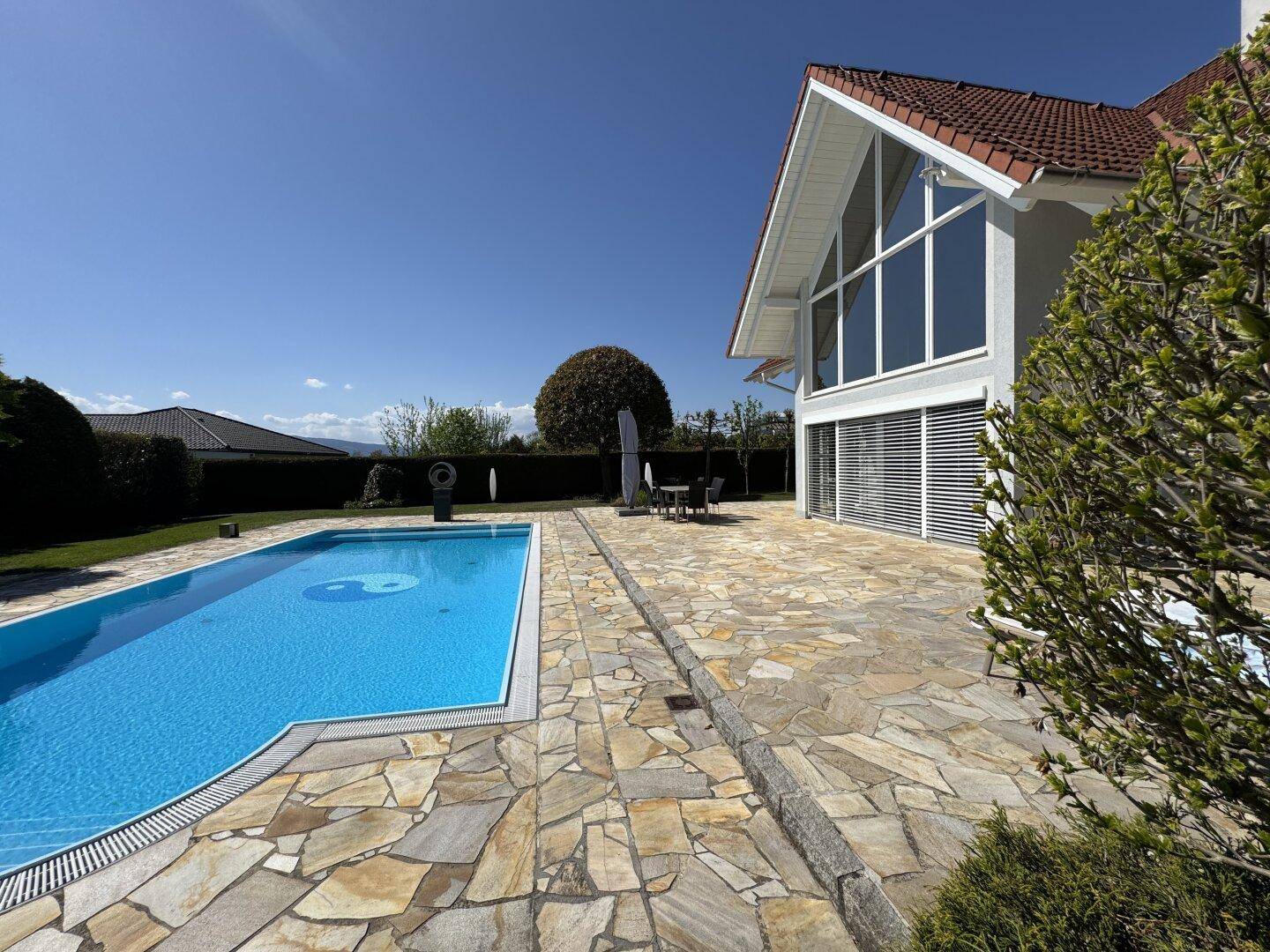 Seitliche Ansicht des Hauses mit Pool und weitläufiger Steinterrasse unter klarem Himmel.