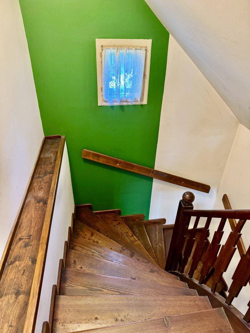 Holztreppe mit Geländer und einer grünen Akzentwand, die zum oberen Stockwerk führt.