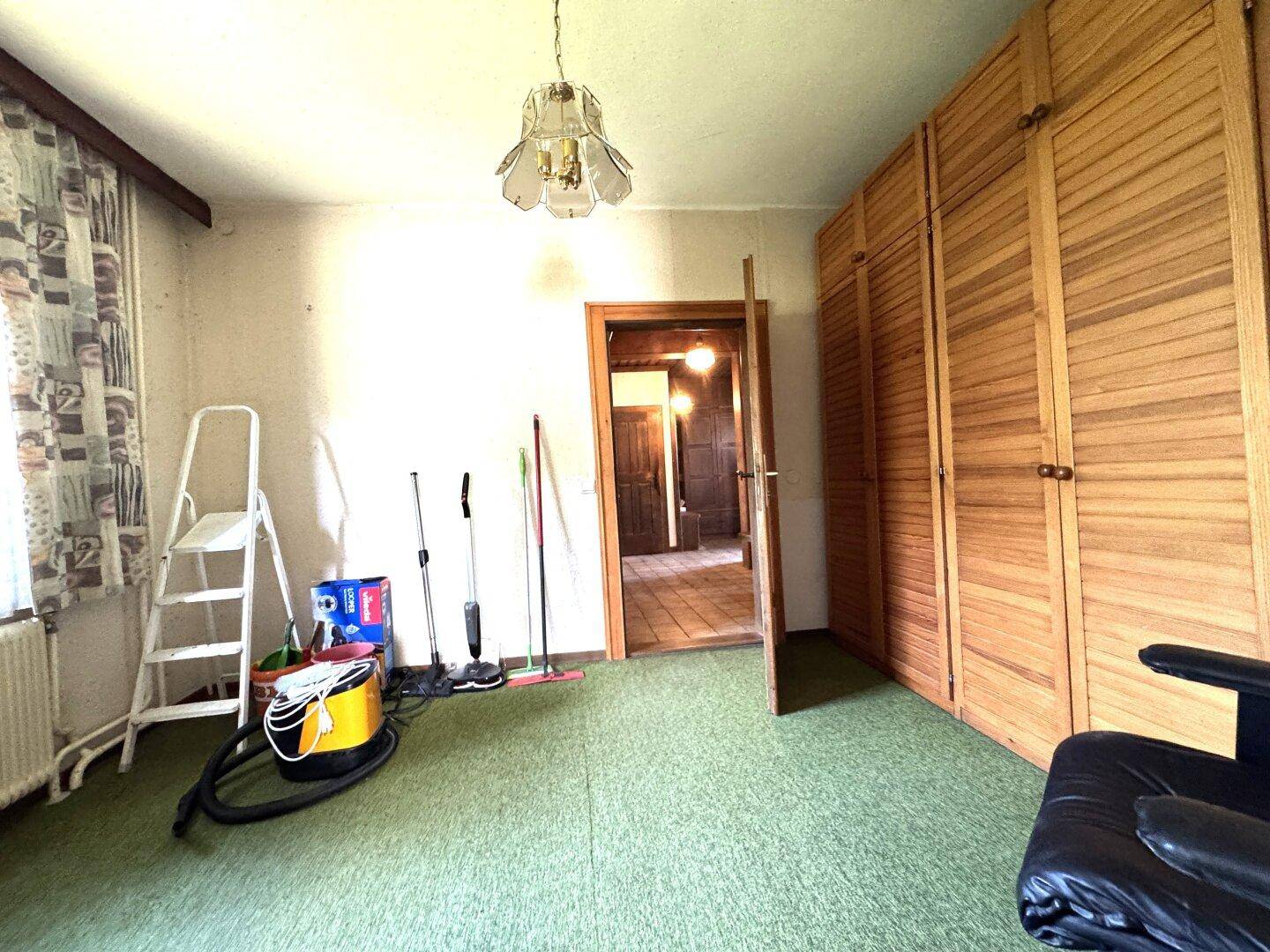 Schlafzimmer mit grünem Teppichboden, Einbauschränken und einem Fenster, das Tageslicht hereinlässt.