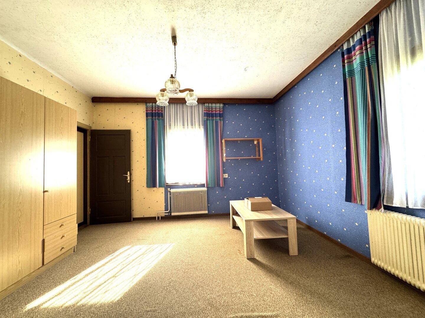 Geräumiges Schlafzimmer mit Teppichboden, Einbauschränken und Fenstern mit bunten Vorhängen.