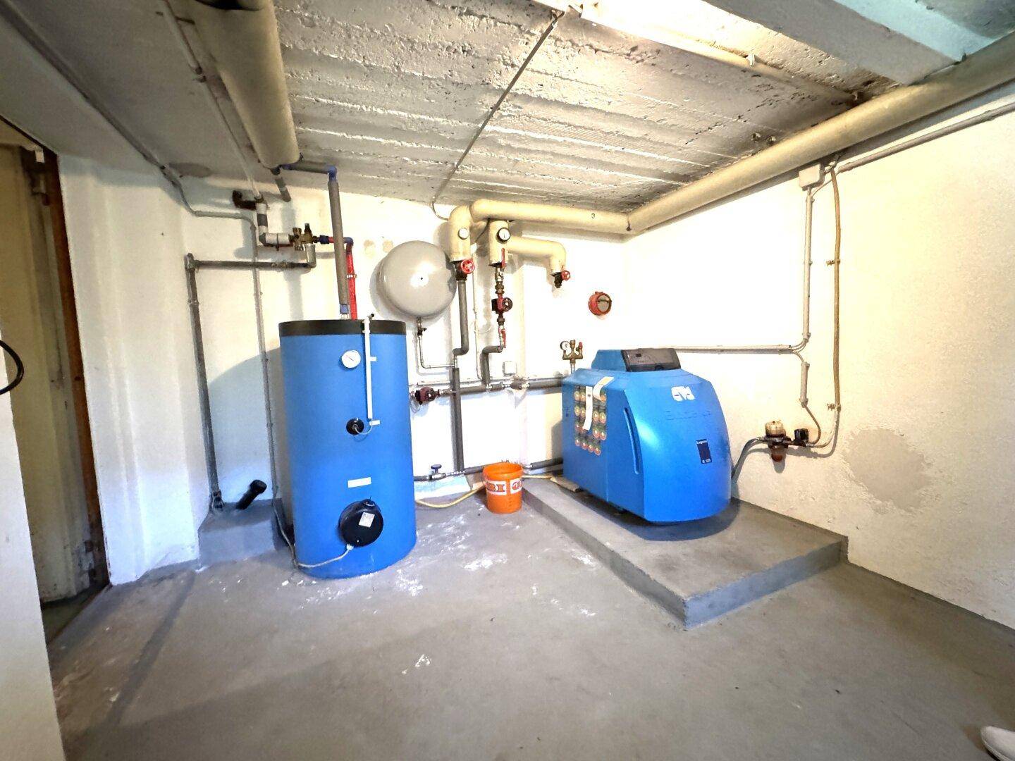 Heizungsraum im Keller mit blauen Warmwasserspeichern und Rohrleitungen an der Decke.