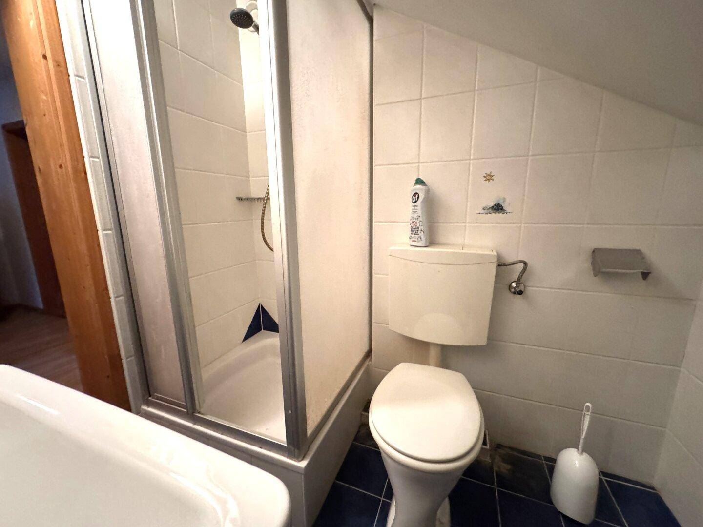 Modernisiertes Badezimmer im Dachgeschoss mit Duschkabine, Toilette und blauen Bodenfliesen.