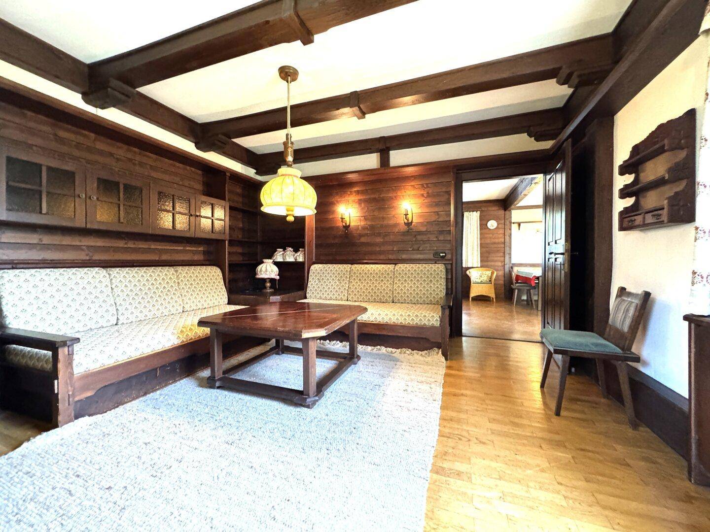 Gemütliches Wohnzimmer mit Holzbalkendecke, Holzvertäfelung und traditionellen Sitzmöbeln im Landhausstil.