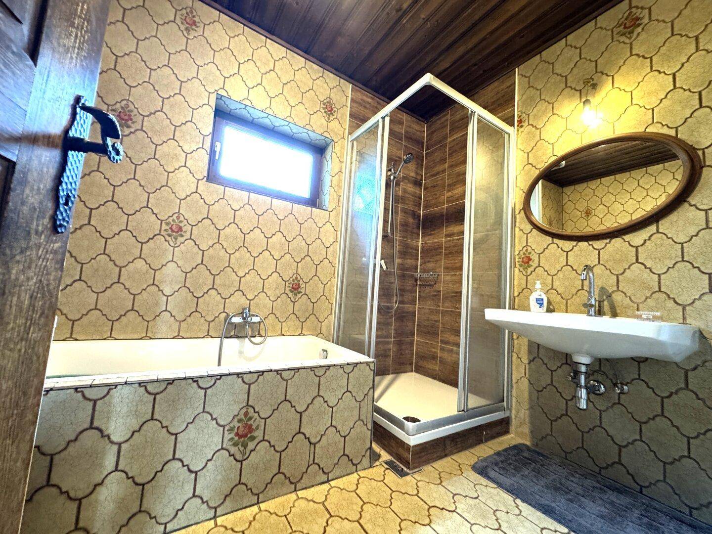 Badezimmer im Retro-Stil mit Badewanne, Duschkabine, Waschbecken und gemusterten Wandfliesen.