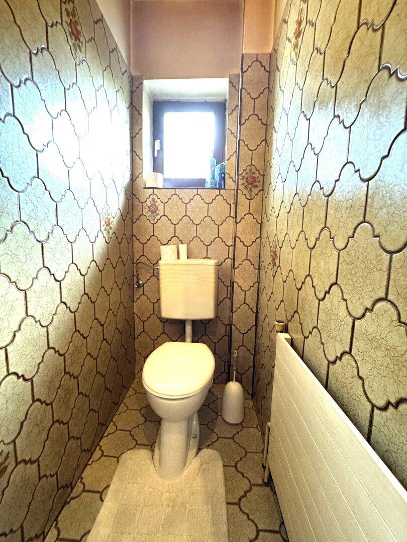 Kleines Gäste-WC mit gemusterten Fliesen, Fenster und einfacher Toilette im 80er-Jahre-Stil.