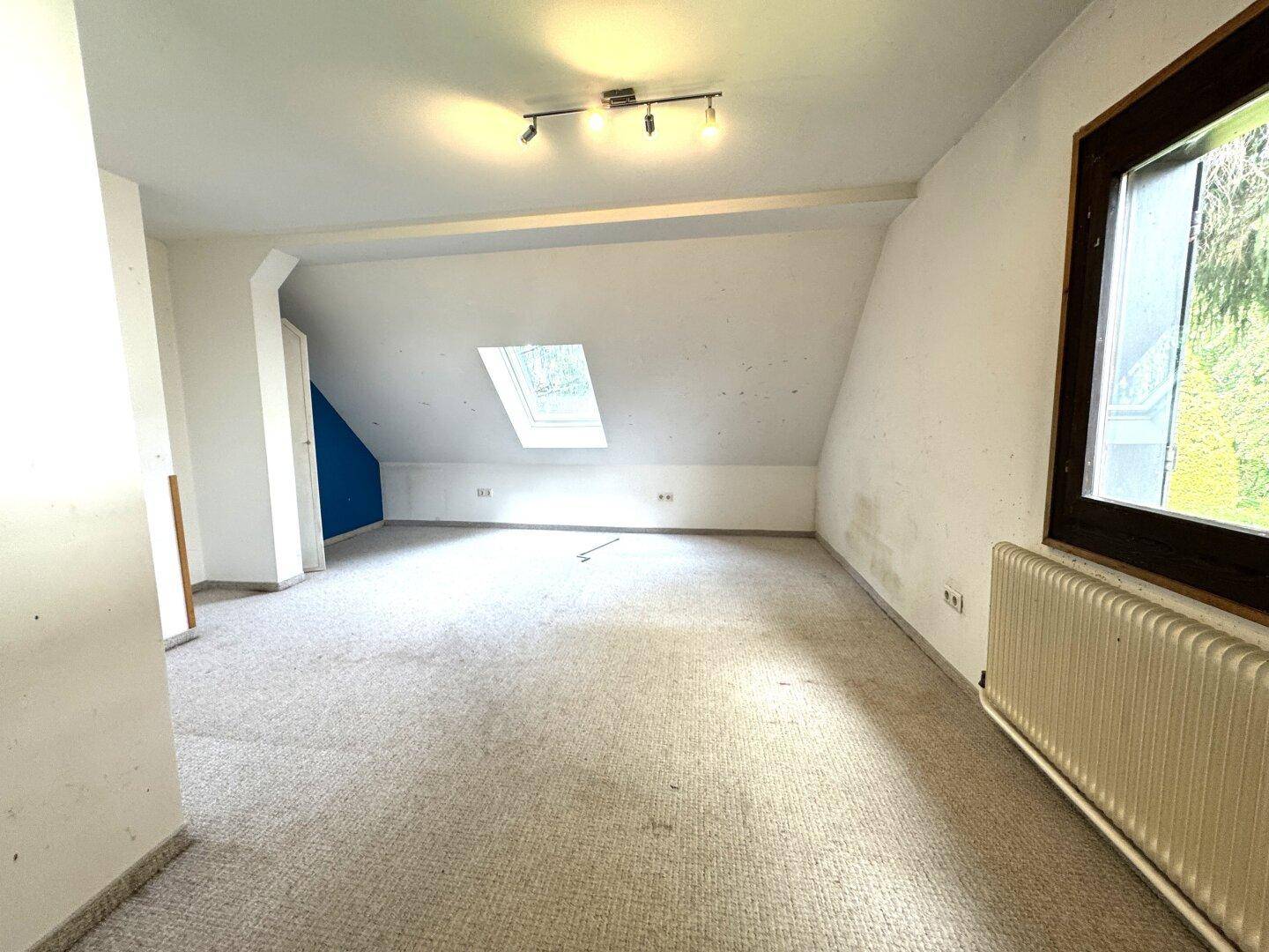 Helles Dachgeschosszimmer mit Teppichboden, Dachschräge und Dachfenster, bietet viel Potenzial.