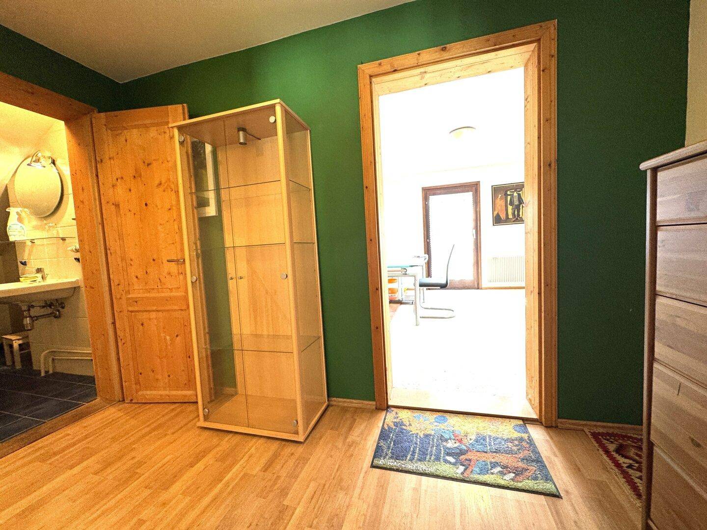 Heller Flur mit Holzboden, grüner Akzentwand und Zugang zu weiteren Wohnbereichen.
