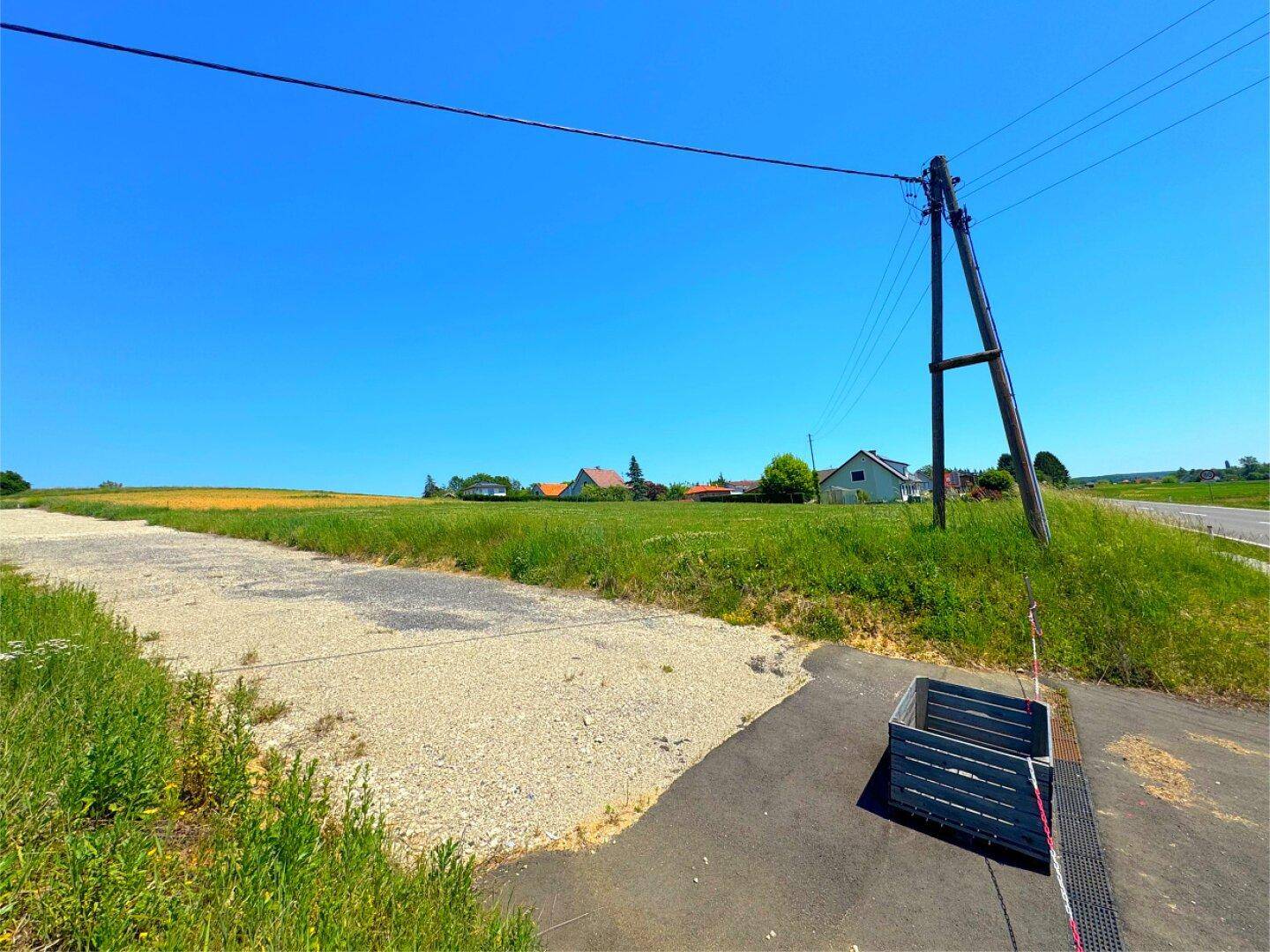 Ländliche Zufahrt neben einer Straße, umgeben von Feldern und einem Strommast.