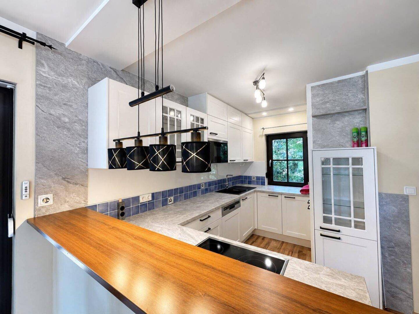 Moderne Küche mit weißen Schränken, Holztheke und blauen Fliesen, offen zum Wohnbereich.