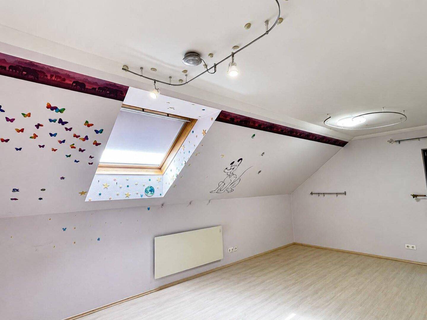 Dachzimmer mit Schrägen, Dachfenster und verspielter Wanddekoration, ideal für Kinder.