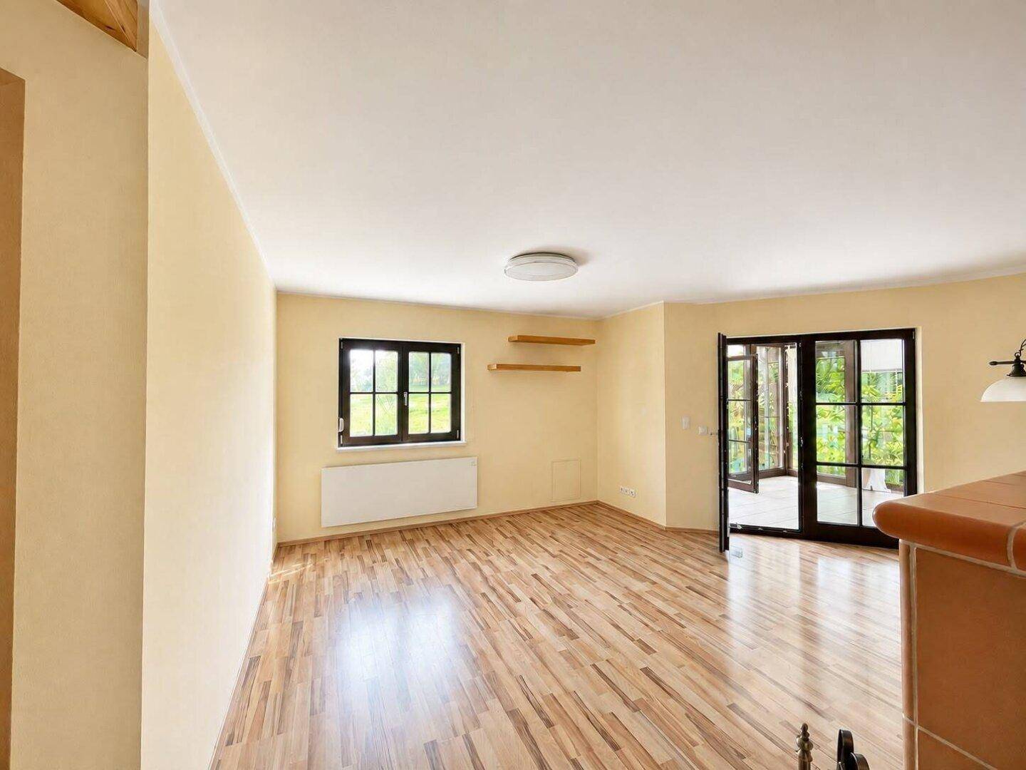 Helles Wohnzimmer mit Parkettboden und großen Fenstertüren, die viel Tageslicht hereinlassen.