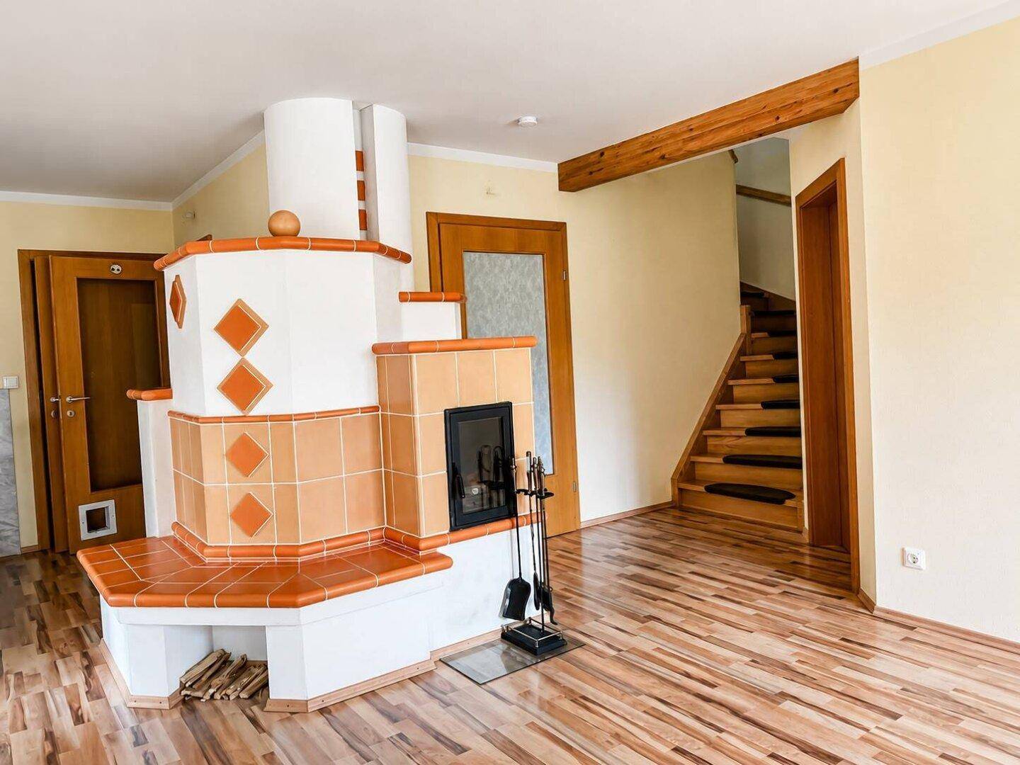 Gemütliches Wohnzimmer mit traditionellem Kachelofen, Holzbalken und Parkettboden.