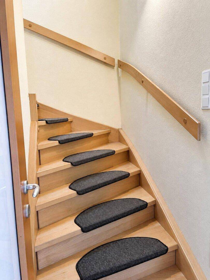 Holztreppe mit Teppichstufen und hellem Holzgeländer, die in die obere Etage führt.