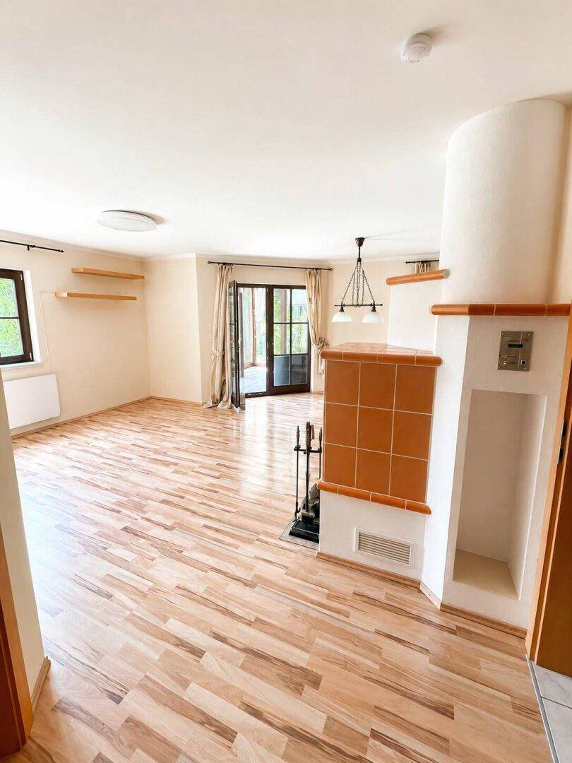 Geräumiges Wohnzimmer mit hellem Parkettboden, Kachelofen und Zugang zum Wintergarten.