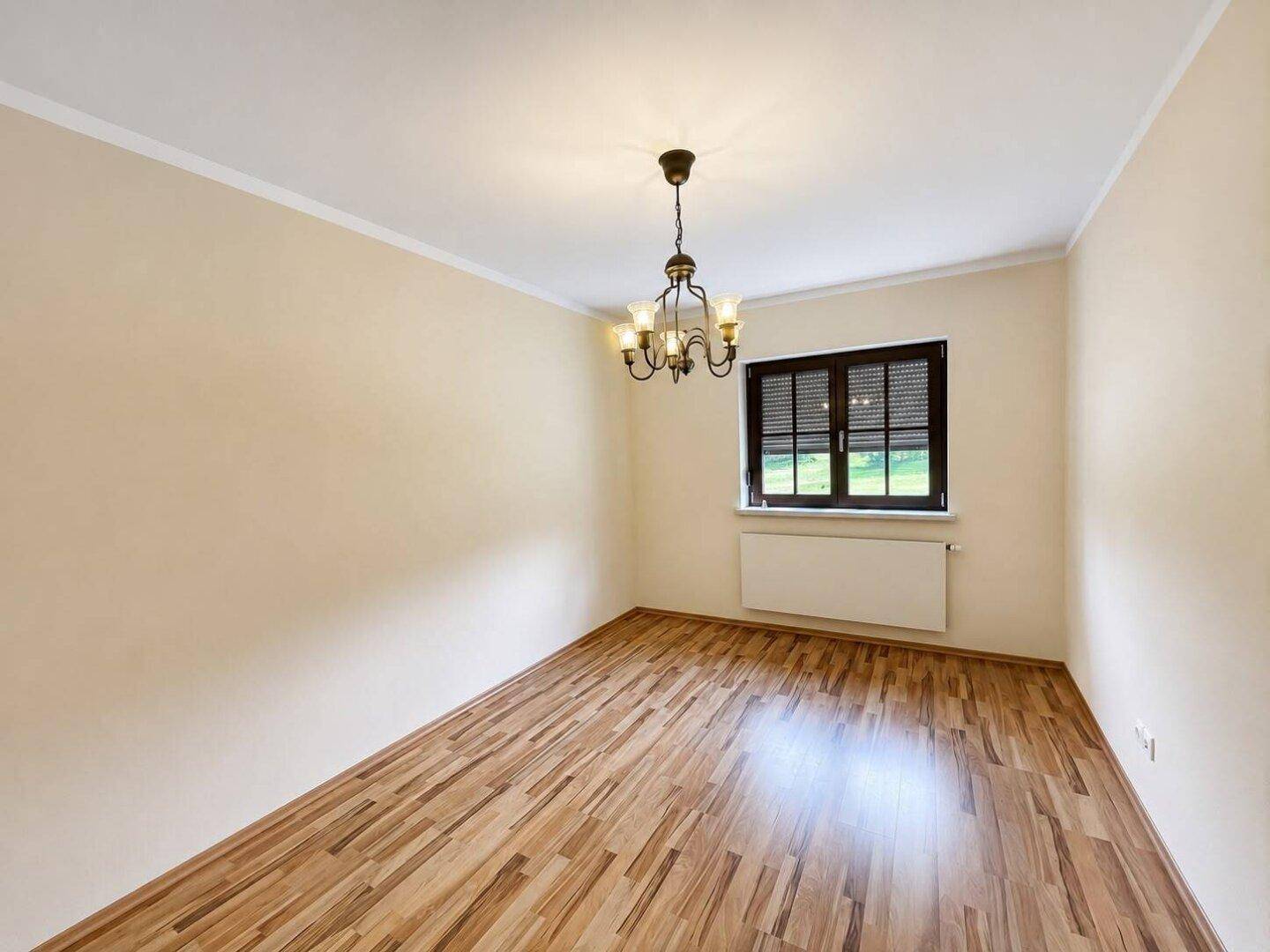 Helles Zimmer mit Parkettboden, Fenster und klassischem Kronleuchter, ideal als Esszimmer.