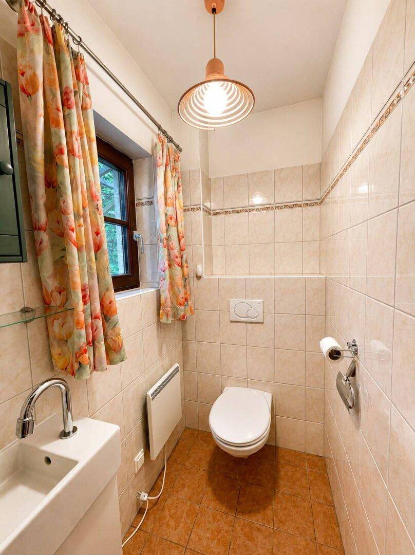 Kleines Gäste-WC mit beigefarbenen Fliesen, Fenster und modernem Waschbecken.