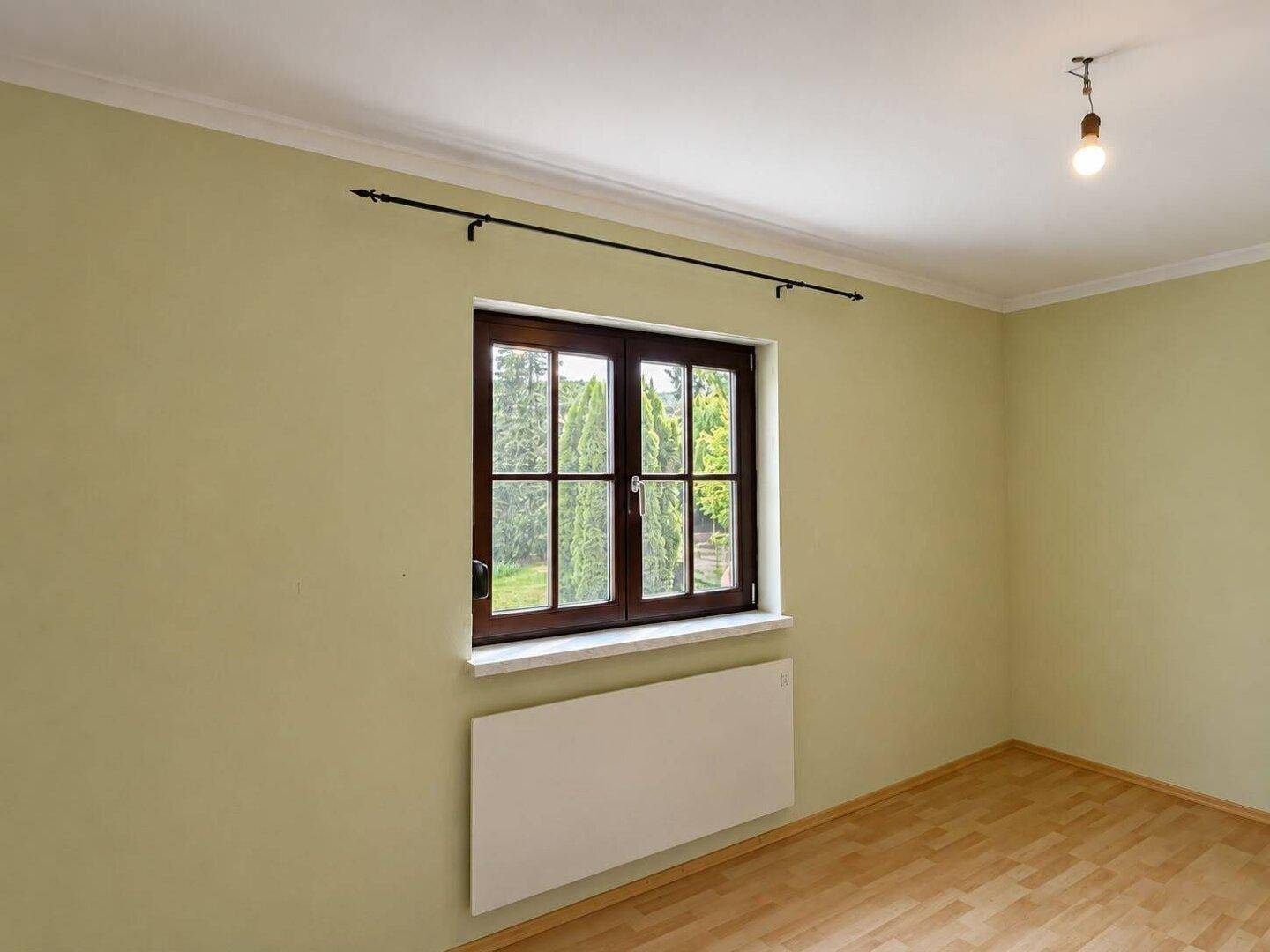 Ruhiges Zimmer mit hellem Parkettboden, grünen Wänden und Blick ins Grüne durch das Fenster.