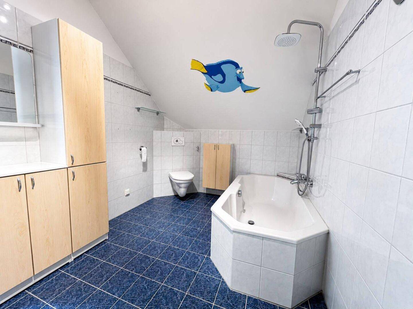 Geräumiges Badezimmer im Dachgeschoss mit blauen Bodenfliesen, Badewanne und Dusche.