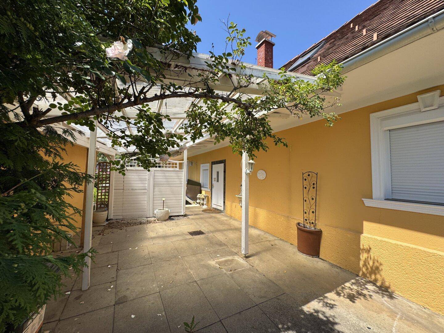 Heller, überdachter Terrassenbereich mit Steinboden und Blick auf den Garten.
