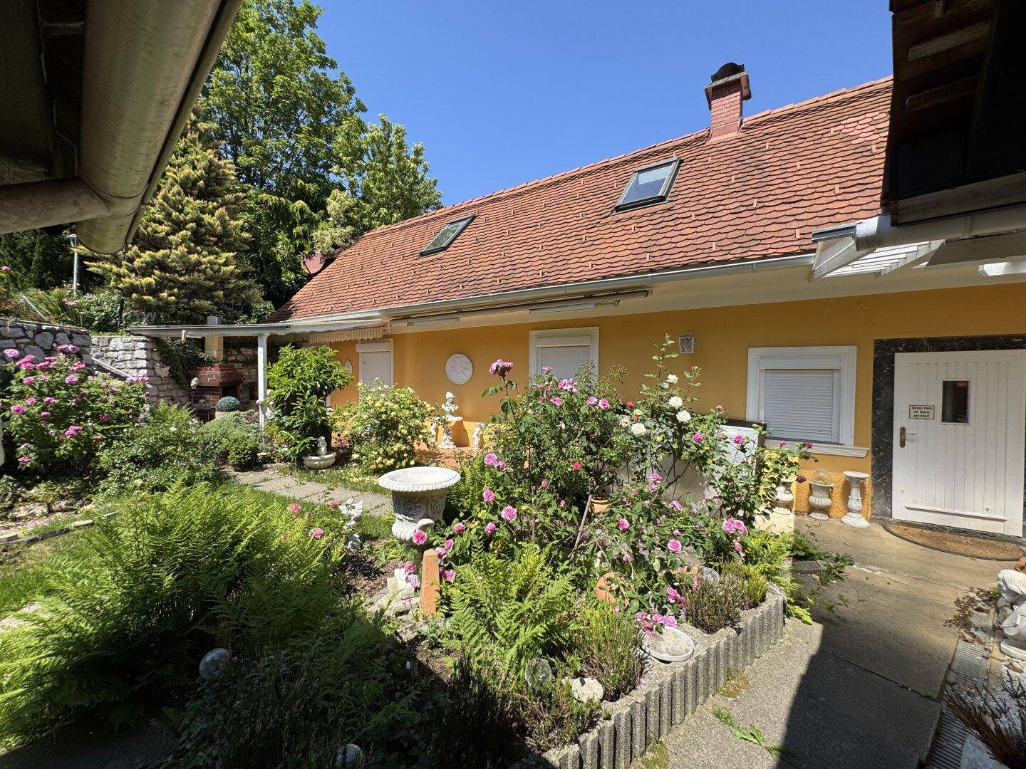 Blühender Rosengarten mit verschiedenen Pflanzen und dem Haus im Hintergrund.