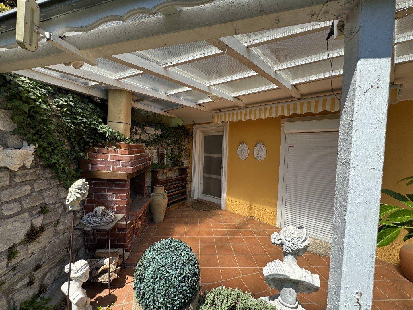 Gemütliche Terrasse mit Terrakotta-Boden, Außenkamin und dekorativen Statuen.