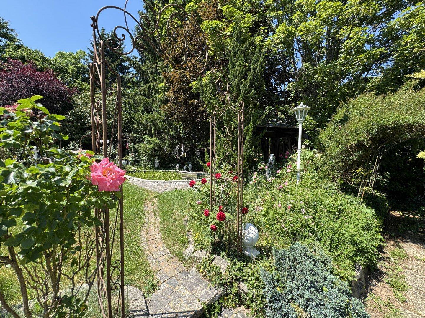 Romantischer Gartenweg mit einem schmiedeeisernen Torbogen und üppigen Rosen.