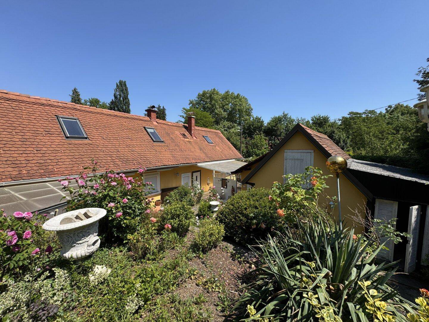 Gepflegter Gartenbereich mit blühenden Pflanzen und zwei Gebäuden im Hintergrund.