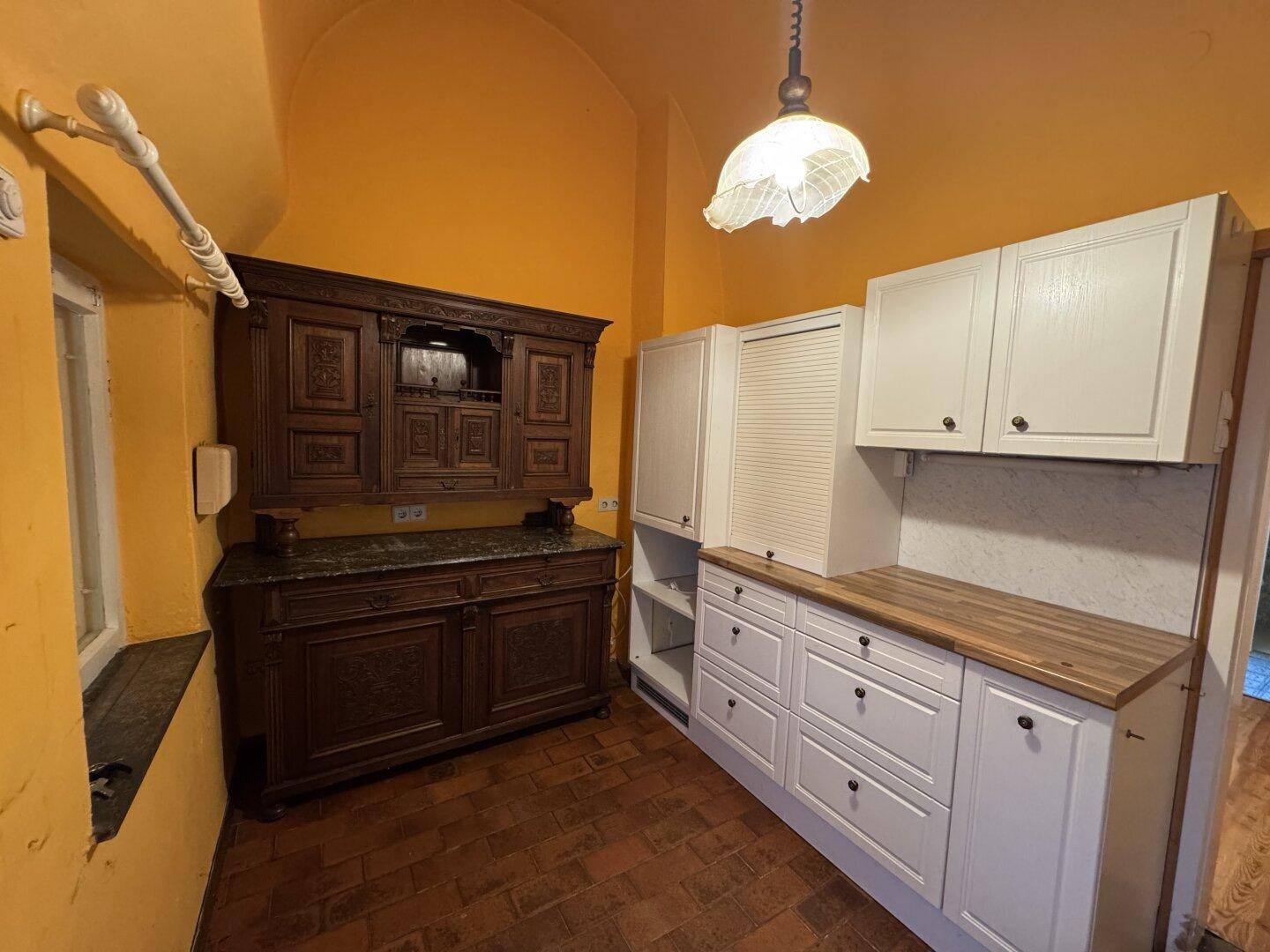 Küche mit traditionellem Holzschrank, modernen weißen Schränken und Terrakotta-Boden.