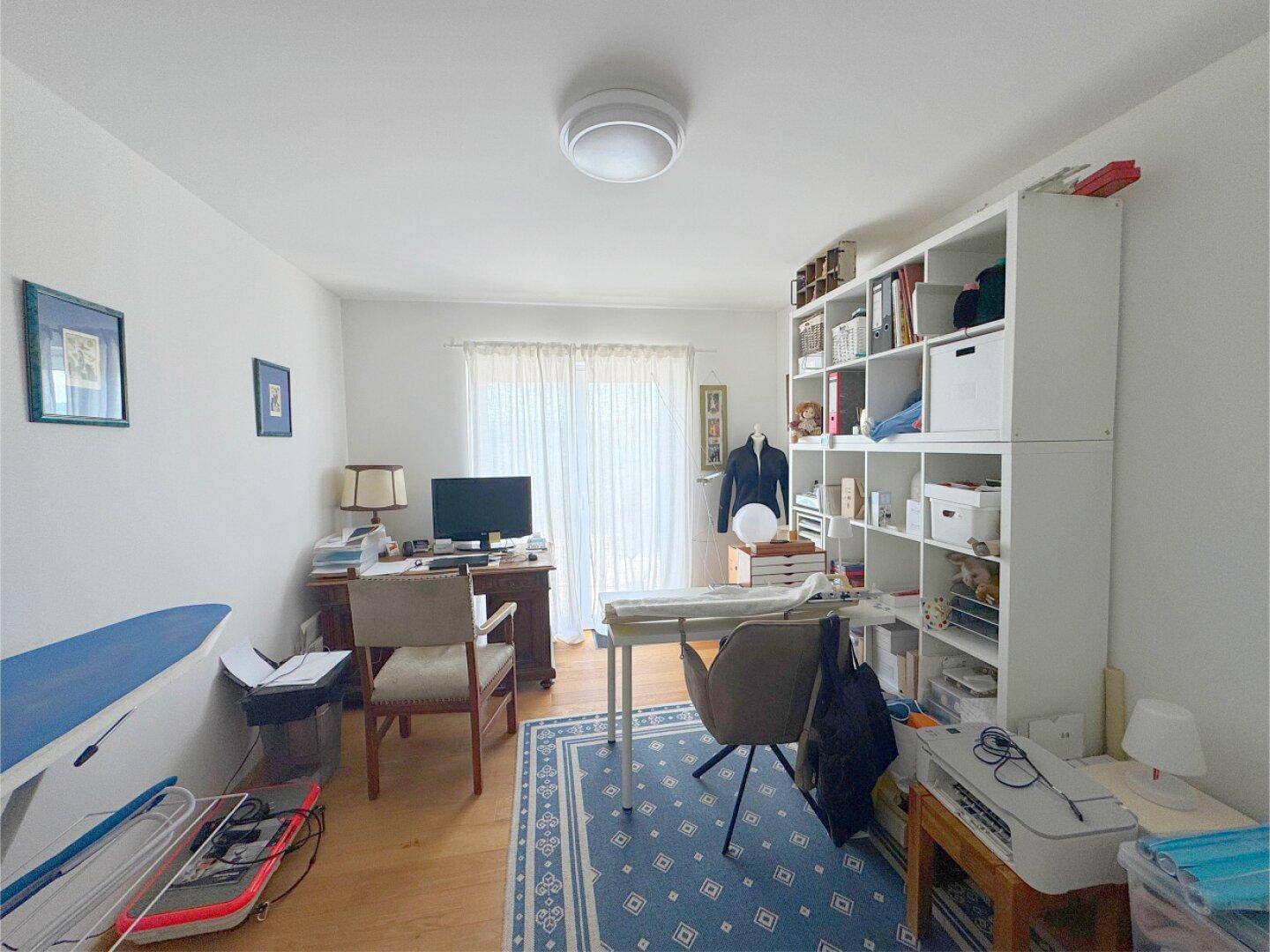 Helles Arbeitszimmer mit Schreibtisch, Regalen und Zugang zu einem Balkon oder Terrasse.