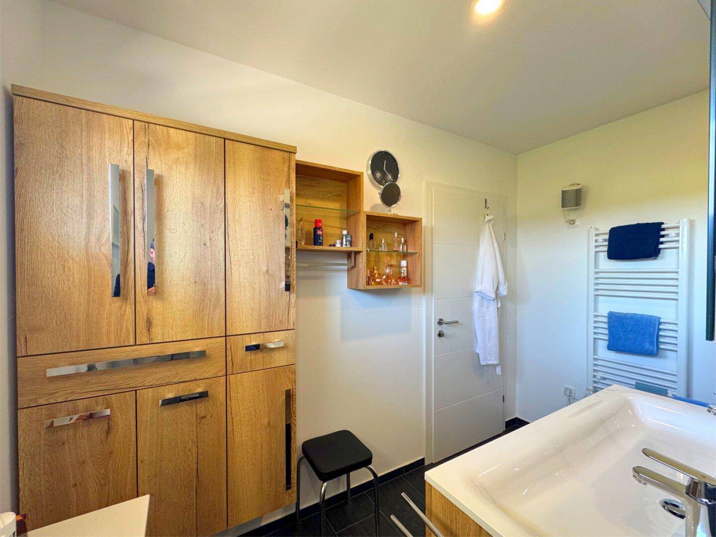 Badezimmer mit geräumigen Holzschränken, beheiztem Handtuchhalter und moderner Einrichtung.