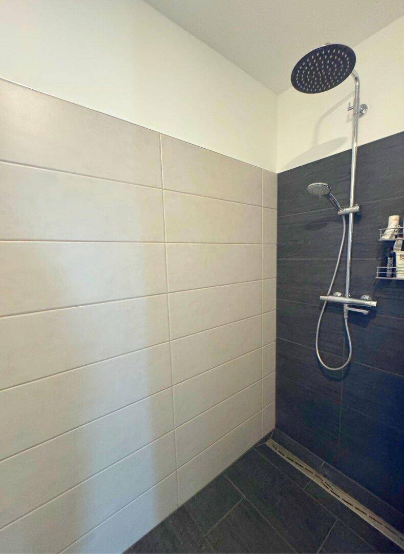 Moderne begehbare Dusche mit Regenduschkopf und großformatigen Fliesen.