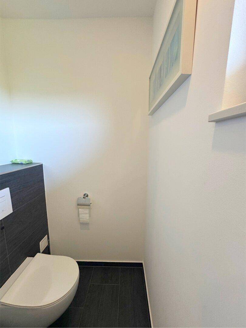 Separates WC mit wandhängender Toilette und dunklen Bodenfliesen.