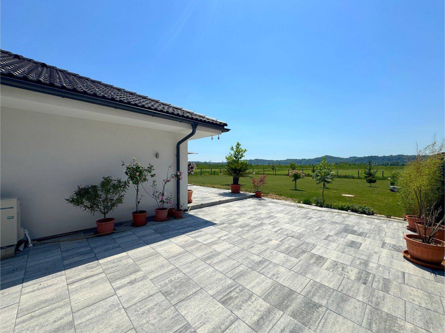 Gepflasterter Bereich neben dem Haus mit Topfpflanzen und weitem Blick in die grüne Landschaft.
