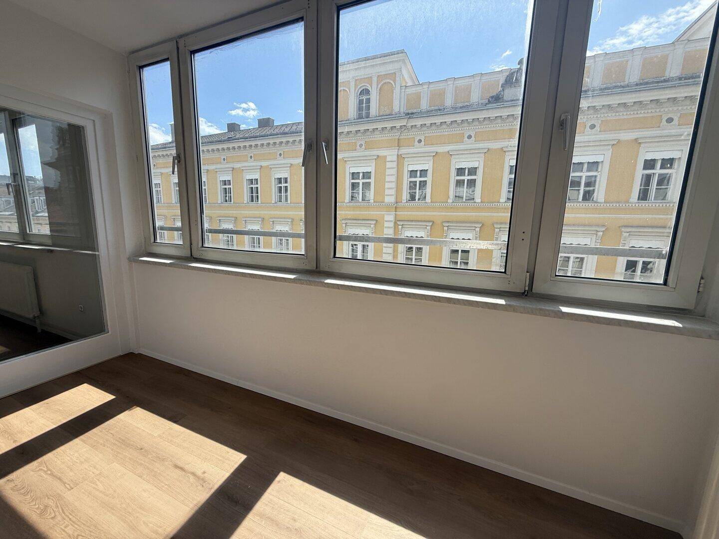 Verglaste Loggia mit Holzboden und weitem Blick auf die umliegenden Gebäude, ideal für entspannte Stunden.