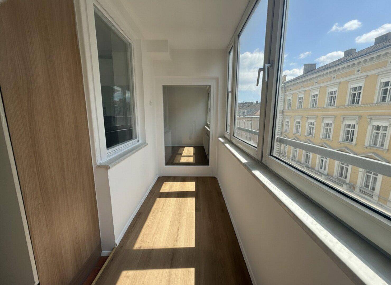 Schmale, verglaste Loggia mit Holzboden und hellem Tageslicht, ideal als Erweiterung des Wohnraums.