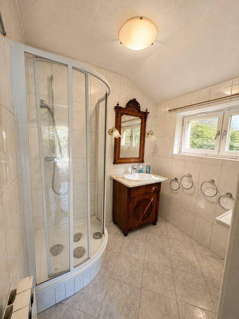 Badezimmer mit Duschkabine, Einzelwaschbecken und Fenster für Tageslicht.