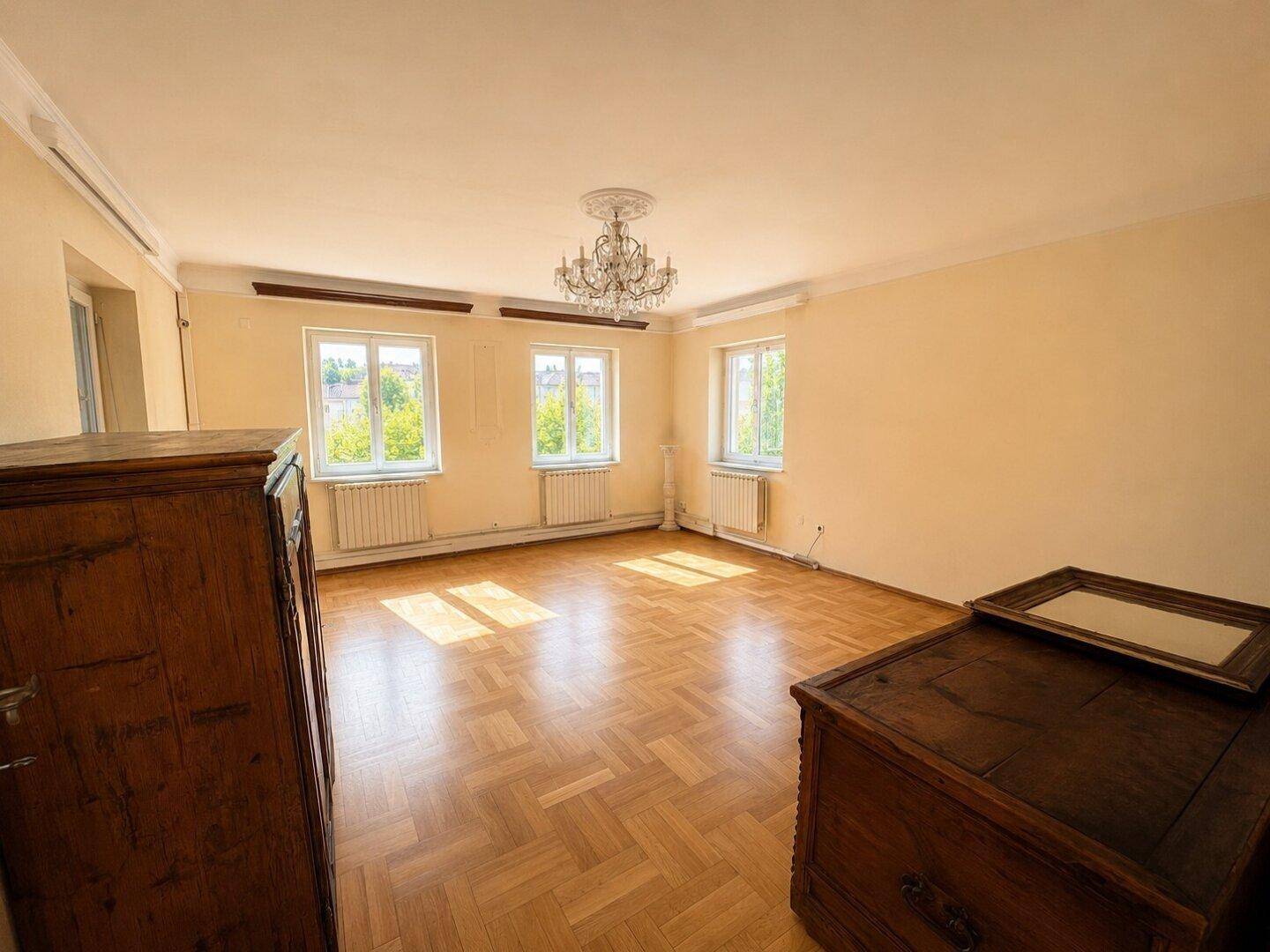 Geräumiges Zimmer mit Fischgrätparkett, hohen Decken und Kronleuchter.